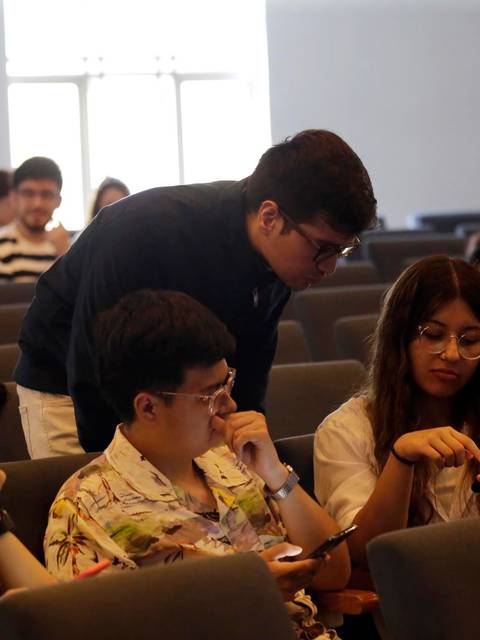 Un grupo de estudiantes conversan y utilizan sus teléfonos en un auditorio vacío.