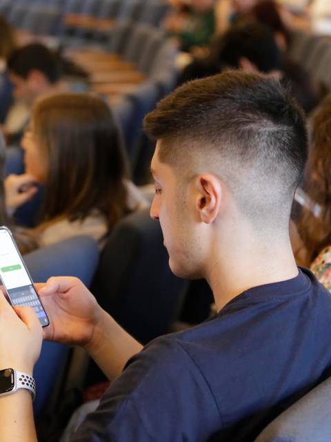 Un grupo de personas sentadas en un auditorio, concentradas en sus teléfonos móviles.