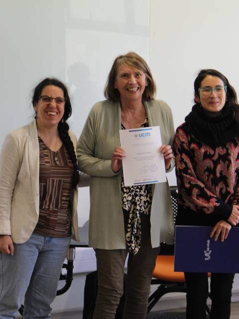 Tres mujeres posando con un certificado en una sala de clases.