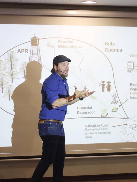 Un presentador expone un tema relacionado con la gestión de recursos hídricos frente a una proyección en una sala de conferencias.