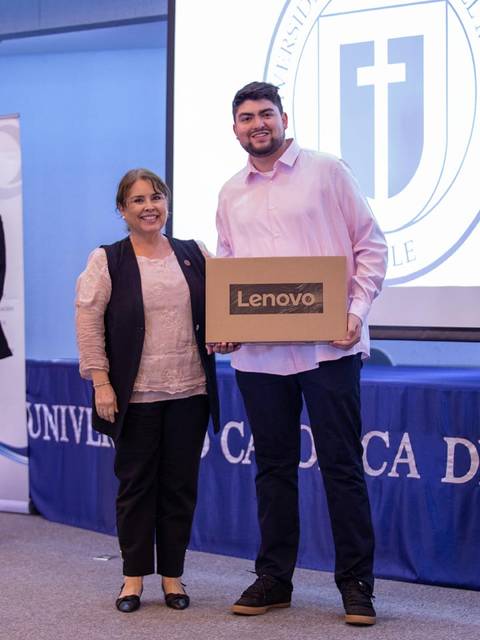 Un estudiante recibe un premio de Lenovo de manos de una profesora en un acto académico en la universidad.