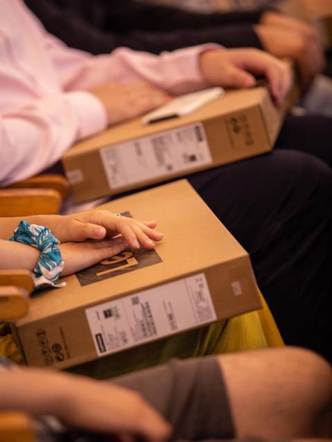 Un grupo de personas sentadas sostiene cajas en sus manos durante un evento.