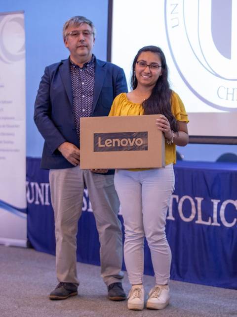 Una mujer sonriente sostiene una caja de Lenovo junto a un hombre en un evento académico.