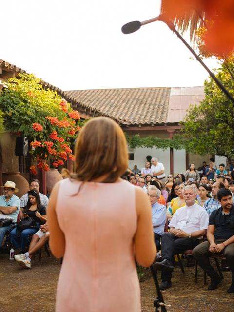 Una mujer de espaldas se prepara para hablar ante un público en un evento al aire libre.