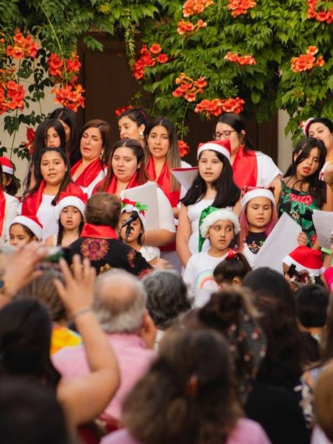 Un grupo de personas canta en un evento festivo, con decoraciones navideñas y un público atento.