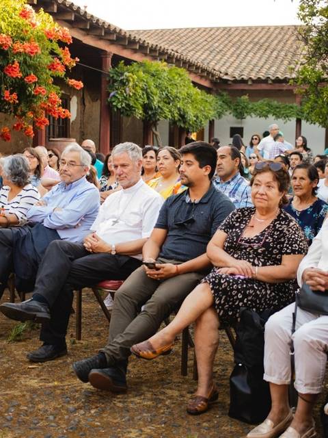 Una multitud de personas sentadas en un evento al aire libre rodeado de vegetación.