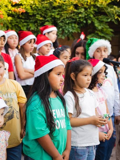 Un grupo de niños en un evento festivo, todos usando gorros navideños.