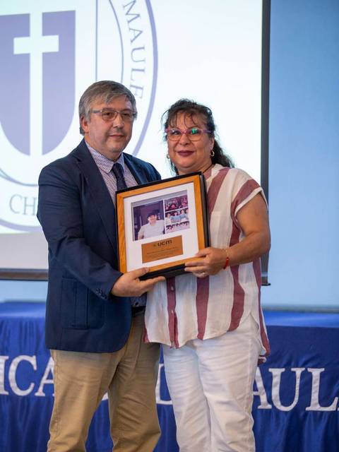 Dos personas sosteniendo un marco con una fotografía en un evento institucional.