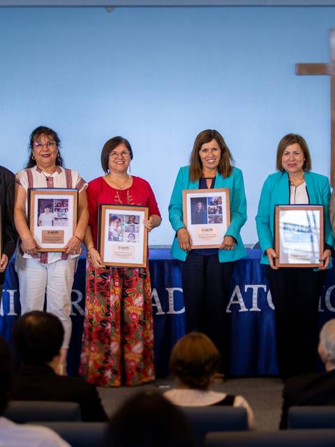 Ceremonia de premiación en la que se destacan a seis personas en un escenario con fondo decorativo y una cruz.