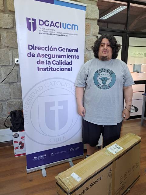 Un hombre de pie junto a un paquete de scooter eléctrico y un cartel de la universidad.