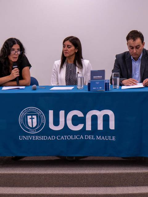 Una mesa de presentación en la Universidad Católica del Maule con tres panelistas discutiendo.