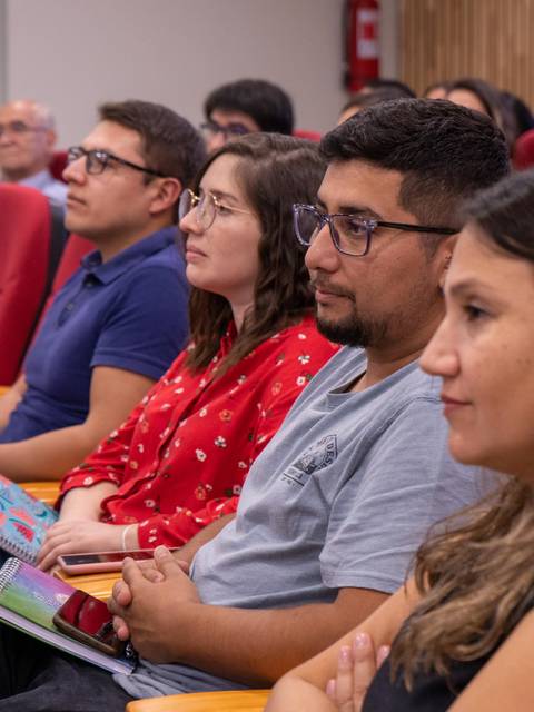 Un grupo de personas sentadas en un auditorio prestando atención a una presentación.