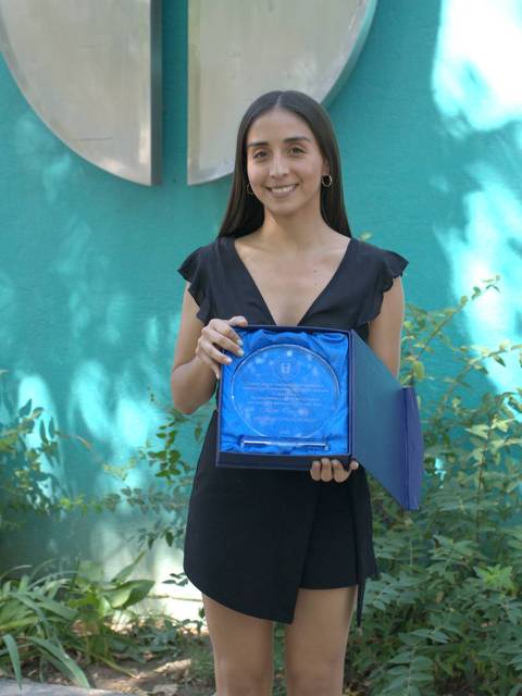 Una joven sonriente sostiene un premio frente a un fondo verde.