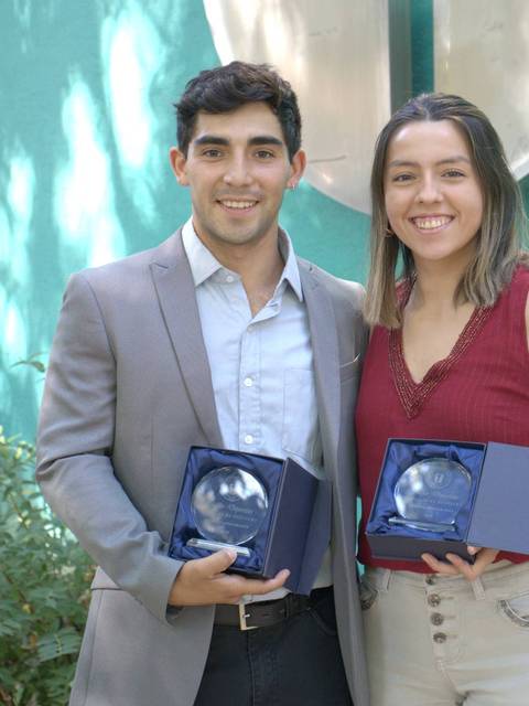 Dos jóvenes posan sonrientes sosteniendo premios en un ambiente natural.