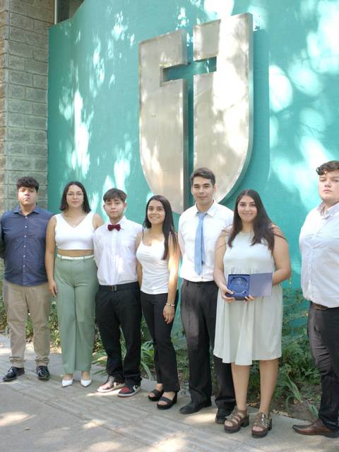 Un grupo de personas posando frente a un edificio con una cruz en la pared.