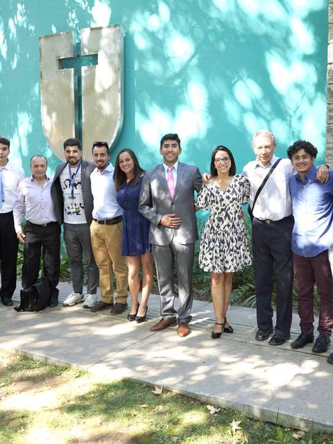 Un grupo de personas posando juntos frente a un edificio con un fondo verde.