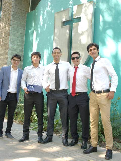 Un grupo de cinco jóvenes posando juntos frente a un edificio de color verde.