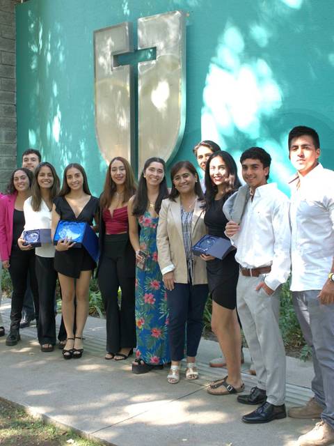 Un grupo de estudiantes posando juntos frente a un edificio con una cruz en la pared.