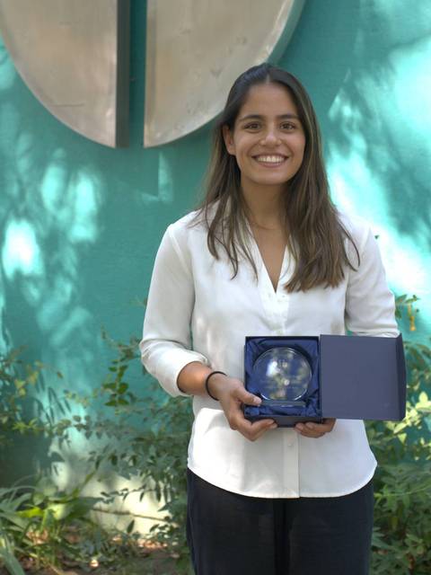 Una mujer sonriente sostiene un premio frente a un fondo verde.