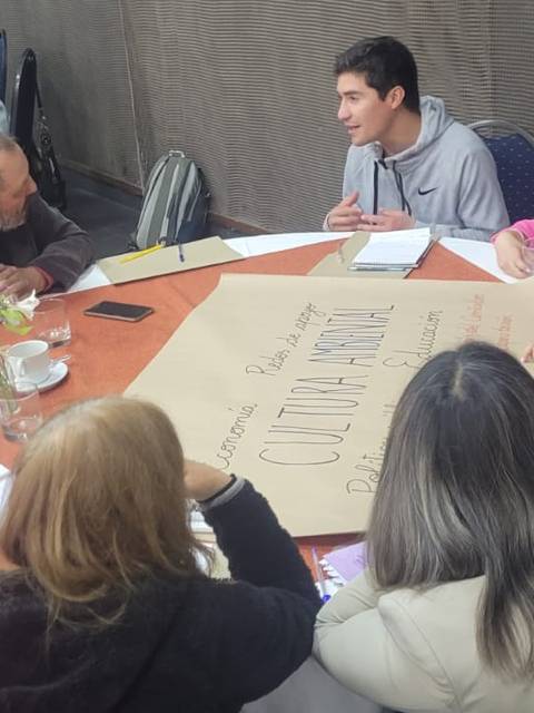 Un grupo de personas discute y colabora alrededor de una mesa en un ambiente de reunión.