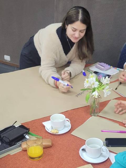 Un grupo de personas está participando en una reunión en una mesa, discutiendo y colaborando mientras disfrutan de bebidas.