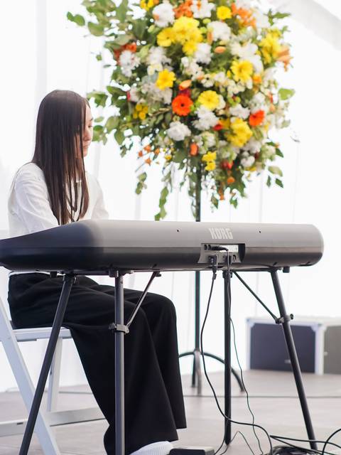 Una joven toca el teclado en un evento decorado con flores coloridas.