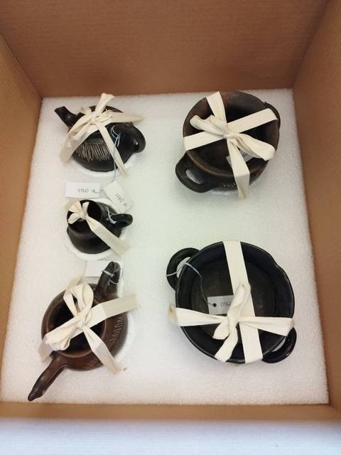 Un conjunto de objetos de cerámica negra envueltos con cintas en una caja de cartón.