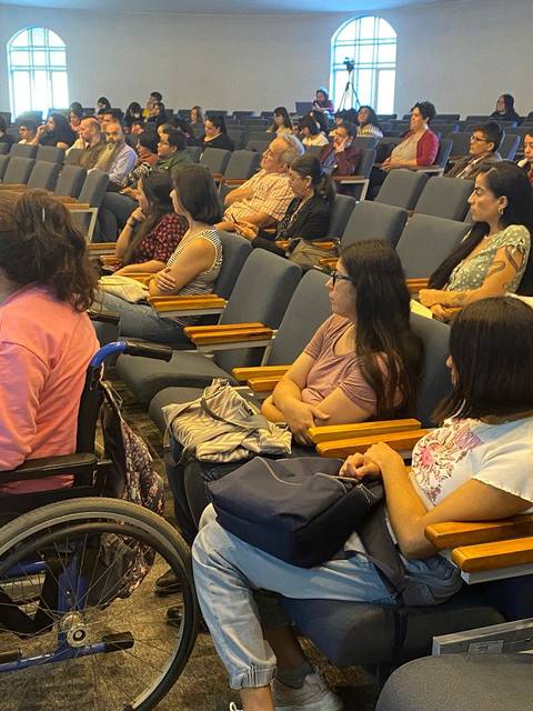Un grupo de personas sentadas en un auditorio, algunas de ellas con discapacidad, prestando atención a un evento.