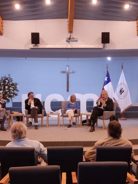Un panel de discusión se lleva a cabo en un auditorio con varias personas sentadas en sillas y un entorno académico.