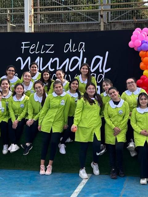 Un grupo de jóvenes sonrientes posa en el Día Mundial de la Mujer, con chaquetas verdes y un fondo colorido.