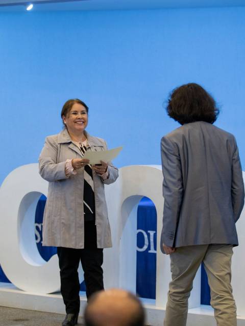 Un evento de entrega de certificados con una mujer sonriendo mientras le entrega un documento a un hombre.