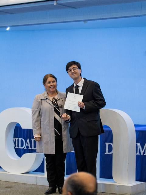 Una ceremonia de entrega de diplomas en la universidad con dos personas posando frente a un cartel que dice UCN.
