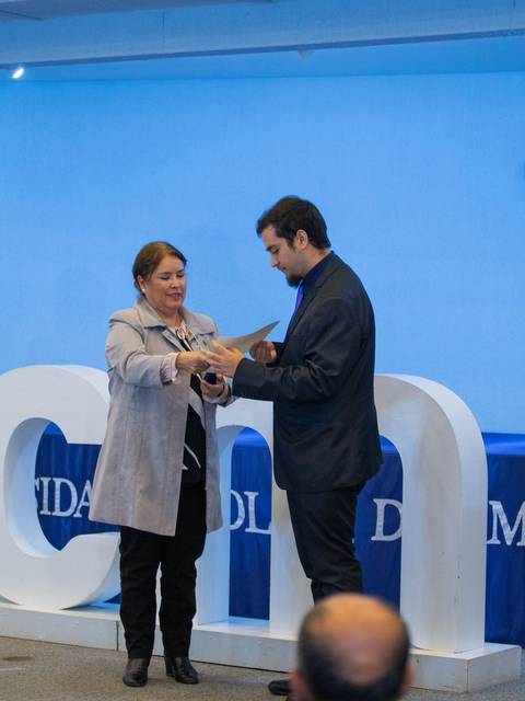 Una mujer y un hombre se encuentran en un evento formal donde están entregando un reconocimiento.