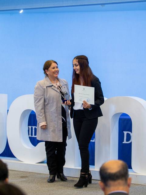 Una ceremonia de entrega de certificados en la que dos mujeres posan sonrientes ante el público.
