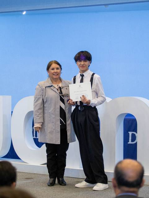Una ceremonia de entrega de certificados en la que un estudiante posa junto a una mujer con un certificado en la mano.