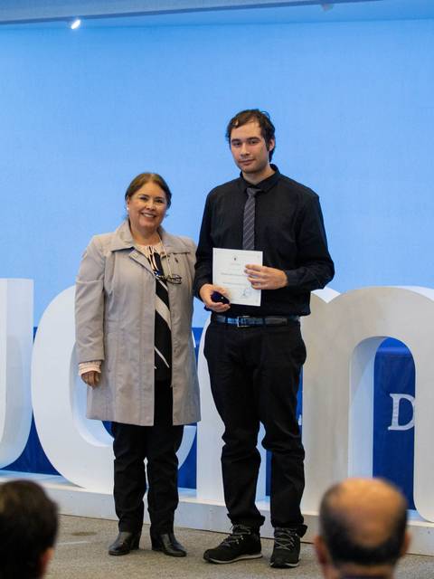 Una ceremonia de entrega de certificados donde una mujer y un hombre posan juntos frente a un fondo decorado.