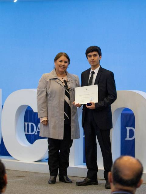 Una mujer y un joven posan juntos sosteniendo un certificado en un evento de graduación.