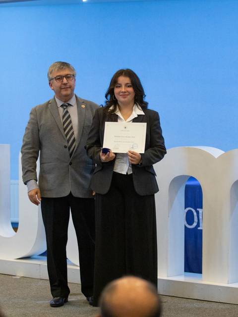 Una mujer sonriente sostiene un certificado junto a un hombre durante un evento en una ceremonia de premiación.