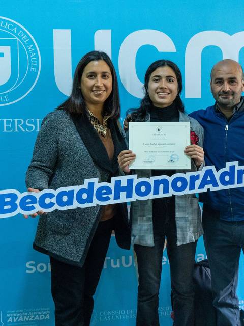 Una estudiante sonriente sosteniendo un certificado junto a dos adultos en un evento de la universidad.