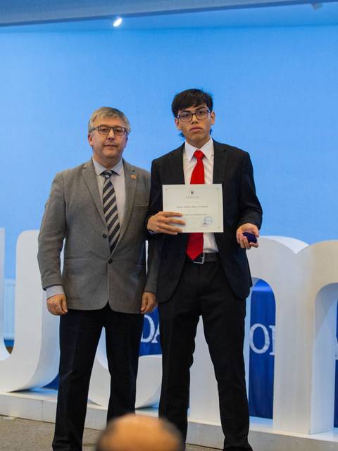 Dos hombres en una ceremonia de entrega de diplomas en un ambiente formal.