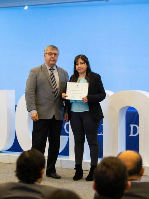 Una mujer recibe un certificado de manos de un hombre en una ceremonia en un auditorio.