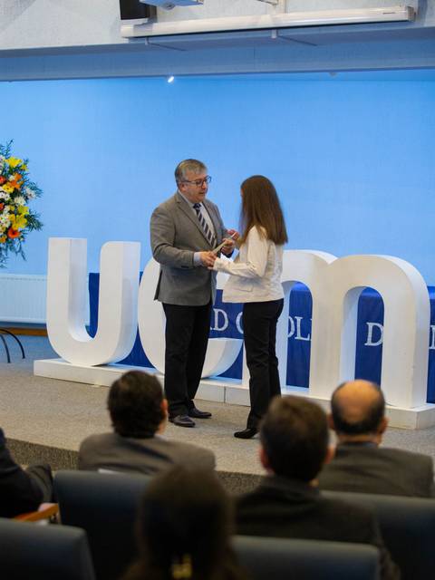 Una ceremonia de entrega de premios en un auditorio con un presidente entregando un reconocimiento a una mujer.