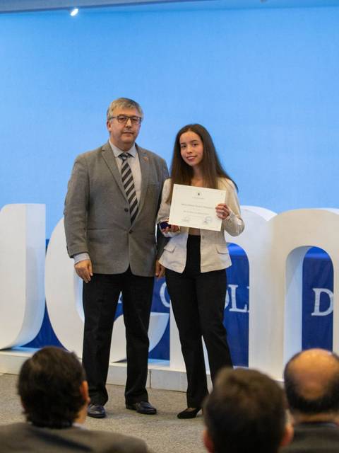Ceremonia de entrega de certificados en la que una joven recibe un reconocimiento de un hombre en un escenario decorado.