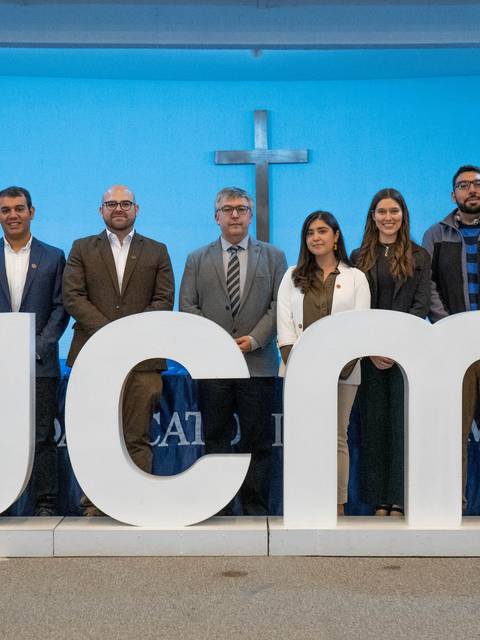 Un grupo de personas posando frente a una gran letra que dice UCM en un ambiente formal.