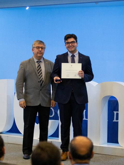 Un estudiante recibe un certificado de manos de un profesor en una ceremonia de entrega de diplomas.