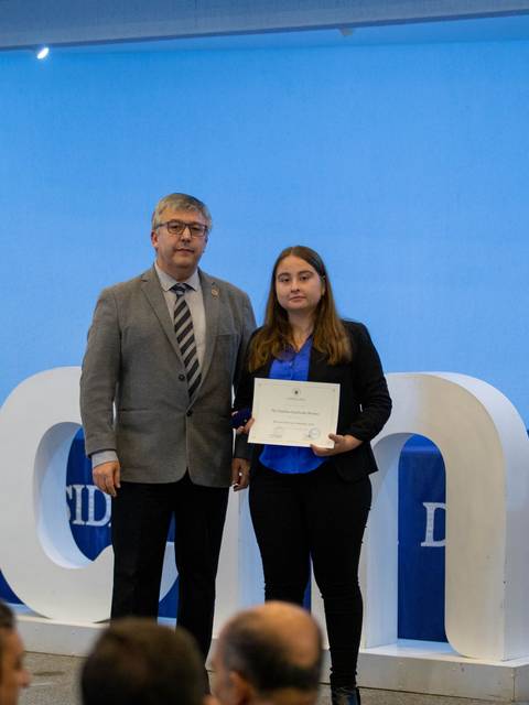 Una ceremonia de entrega de certificado en la que una joven recibe un reconocimiento de un hombre en un evento formal.