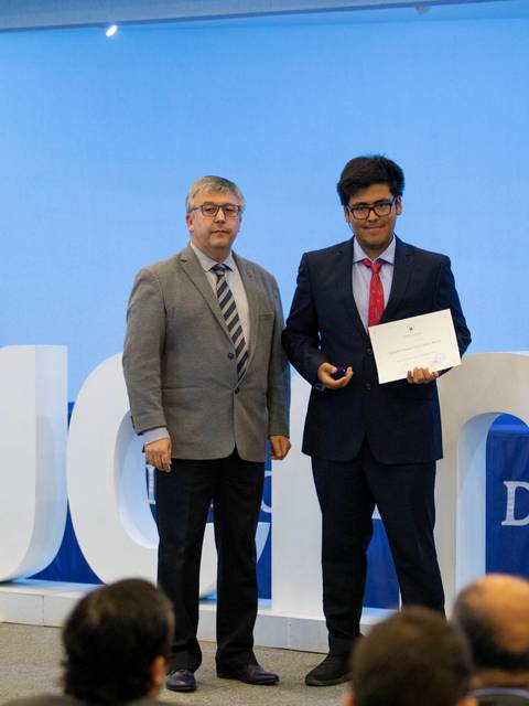 Un estudiante recibe un certificado de manos de un profesor durante una ceremonia en la universidad.