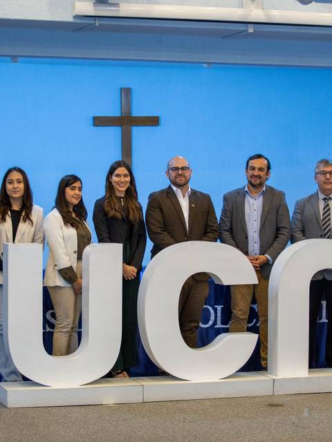 Un grupo de personas posando junto a un letrero que dice 'UCM' en un ambiente de congreso o ceremonia.