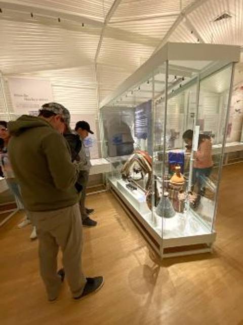 Una exposición en un museo con vitrinas que muestran diversos objetos mientras varias personas observan.