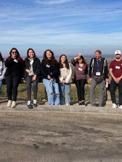 Un grupo de personas posa juntas en un mirador con un paisaje urbano al fondo.